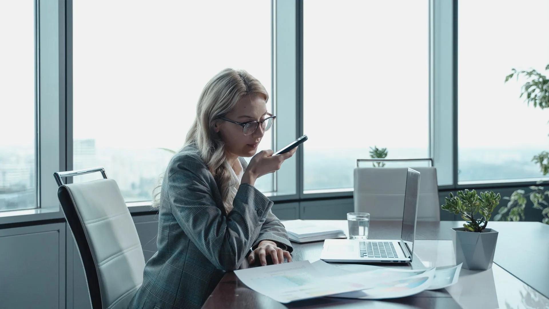 Woman speaking into her phone at a desk — recording a payment by voice in her own language
