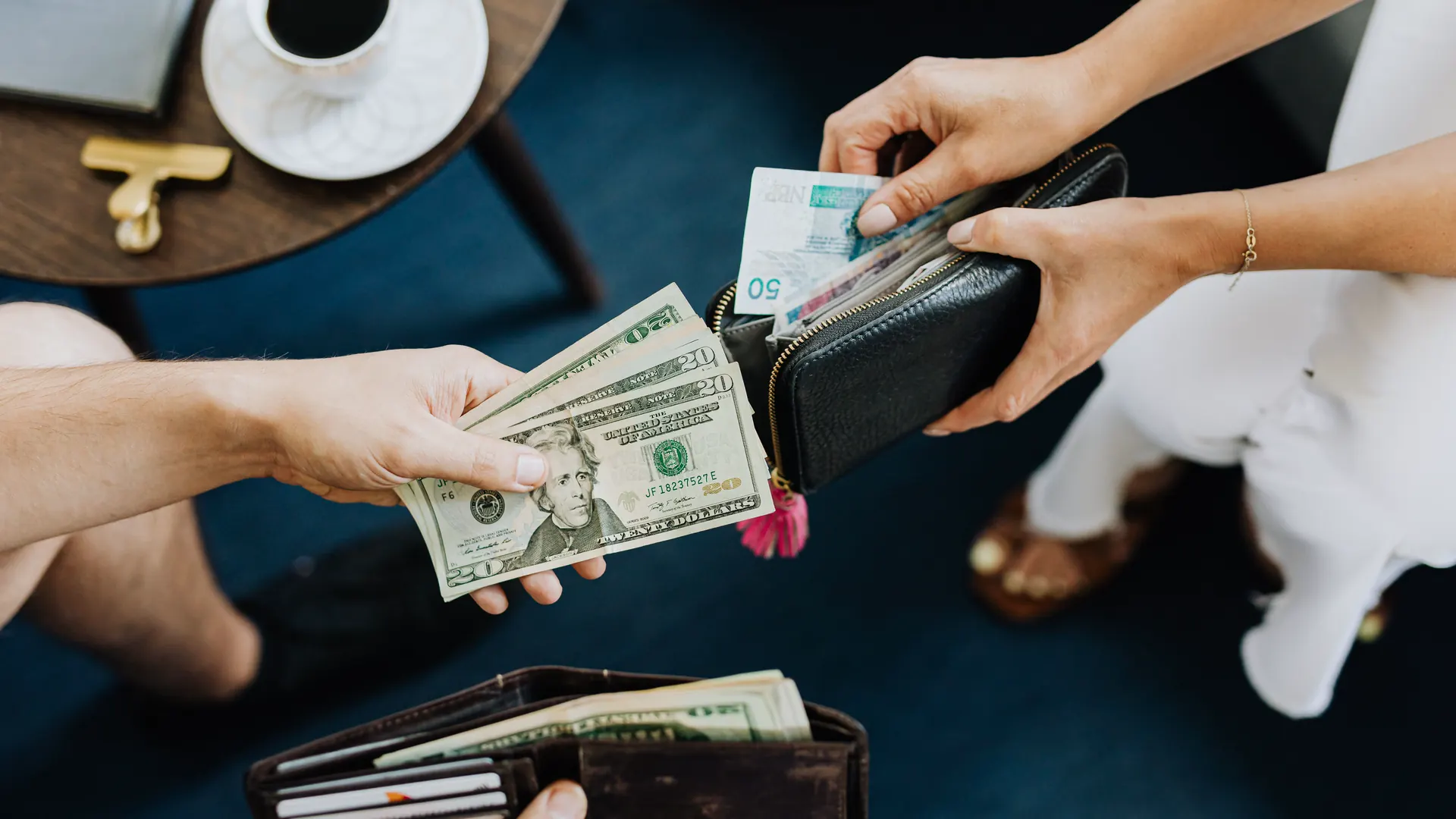 Two people pass cash between an open wallet and a purse